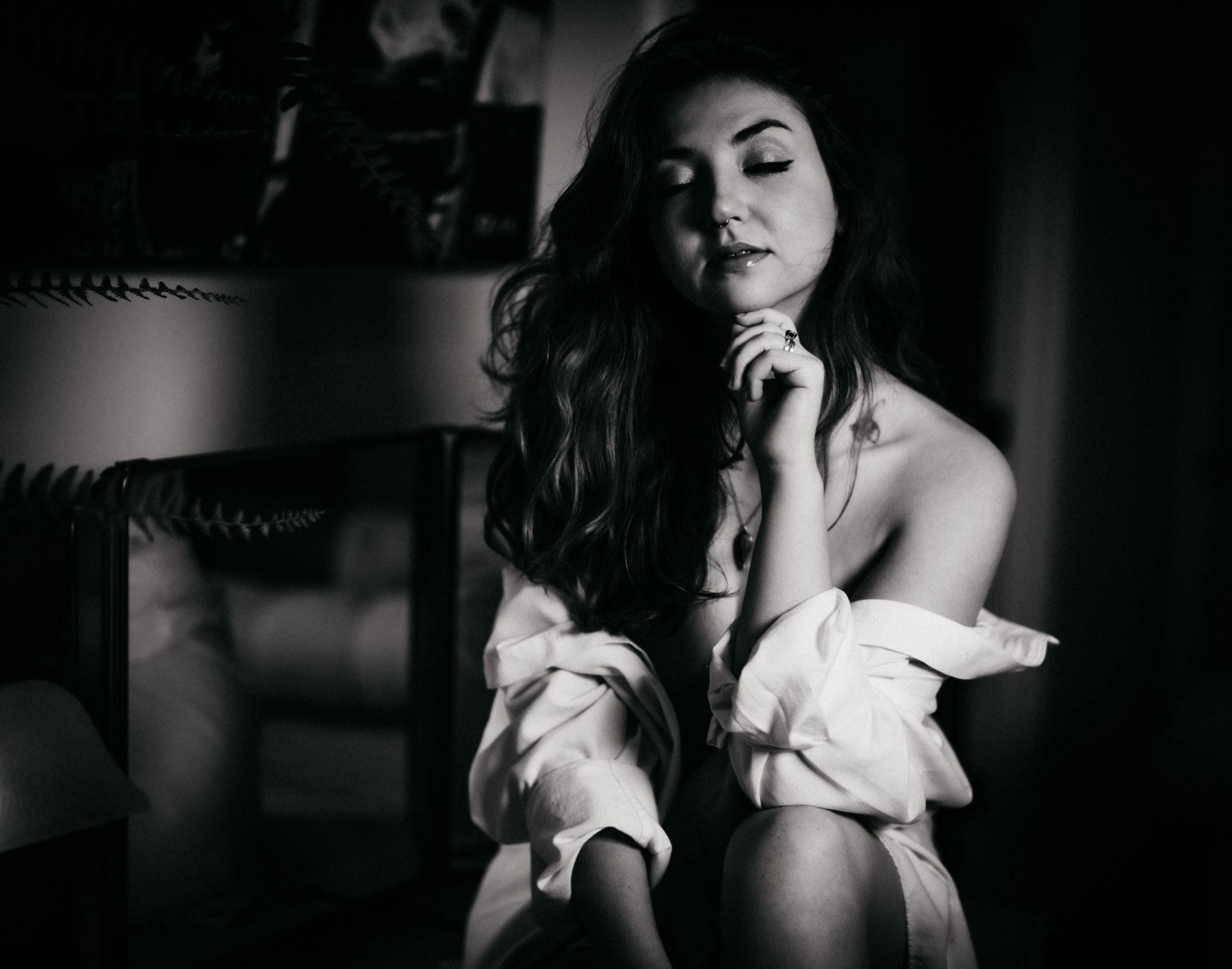 Black and white boudoir portrait of a woman with dark hair, eyes closed, an off-shoulder top falling loose